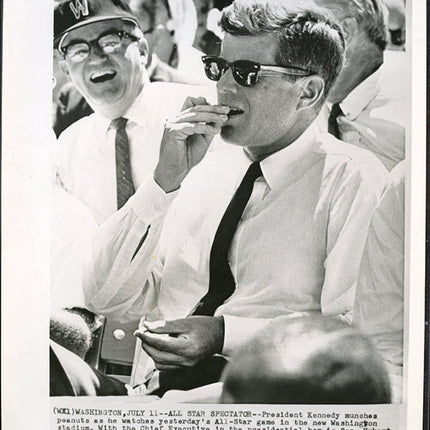 Black and white photograph of JFK eating peanuts at a baseball game, with text overlay.