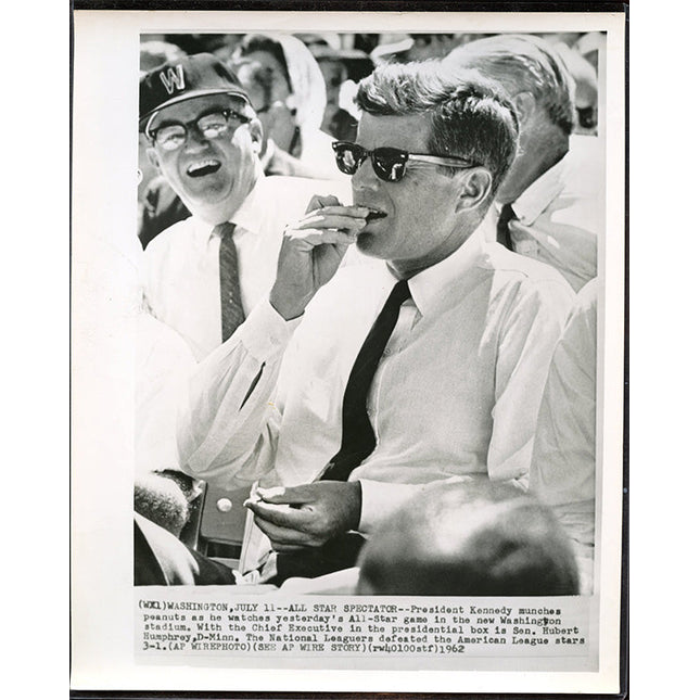 Black and white photograph of JFK eating peanuts at a baseball game, with text overlay.